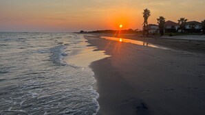 Una platja amb un capvespre, onades oceàniques i cases al fons.