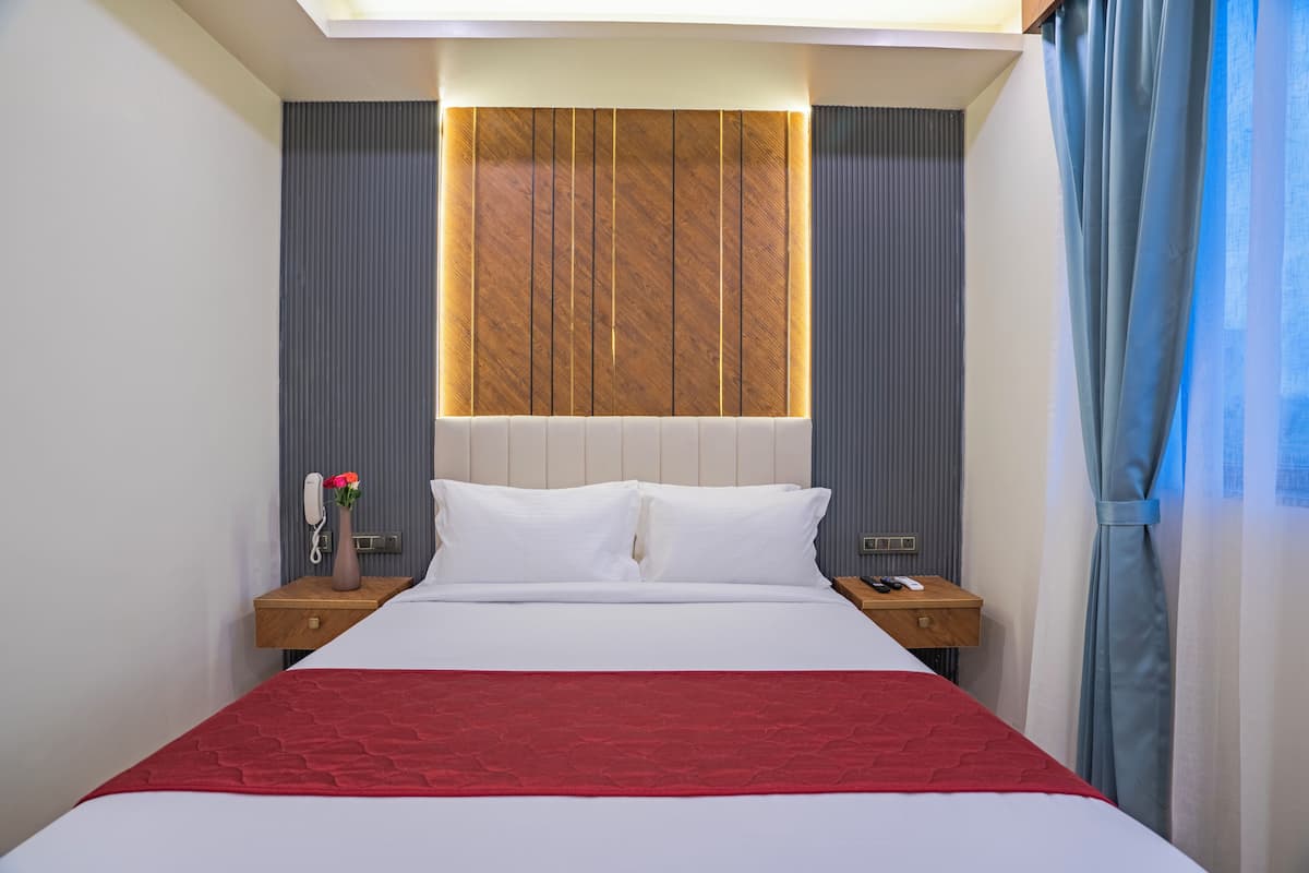 A hotel room with a large bed, wooden headboard, bedside tables, a phone, a vase with flowers, and a red bedspread.
