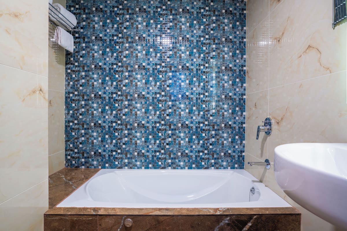 A bathroom with a mosaic tile wall, a white bathtub, and a white sink.