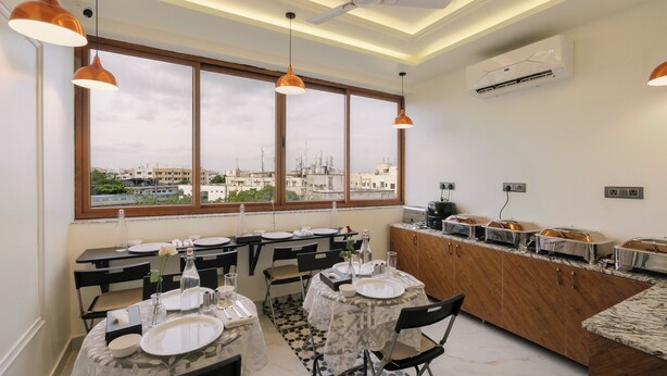 A dining area with tables set for four, a large window with a city view, pendant lights, and an air conditioning unit. - Rcc Hotels Biz stays Begumpet (Hyderabad)