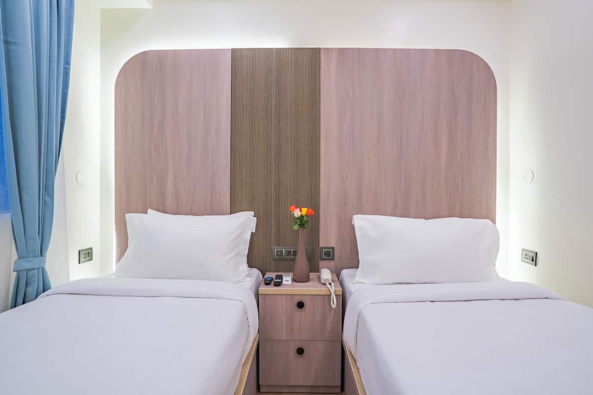 A hotel room with two beds, a nightstand with a phone and a vase of flowers, and a wooden headboard.