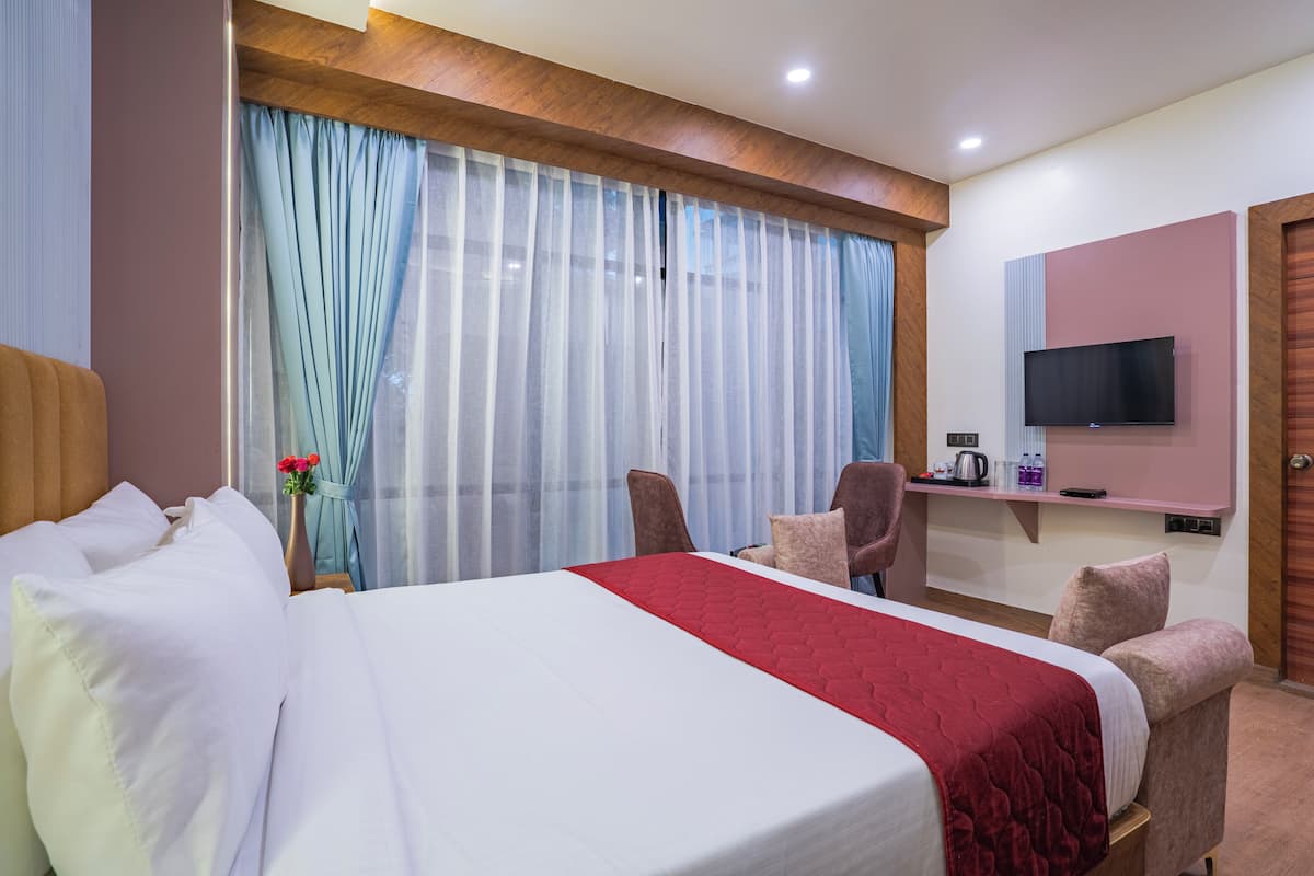 A hotel room with a large bed, a TV mounted on the wall, a desk with a kettle, and a chair.