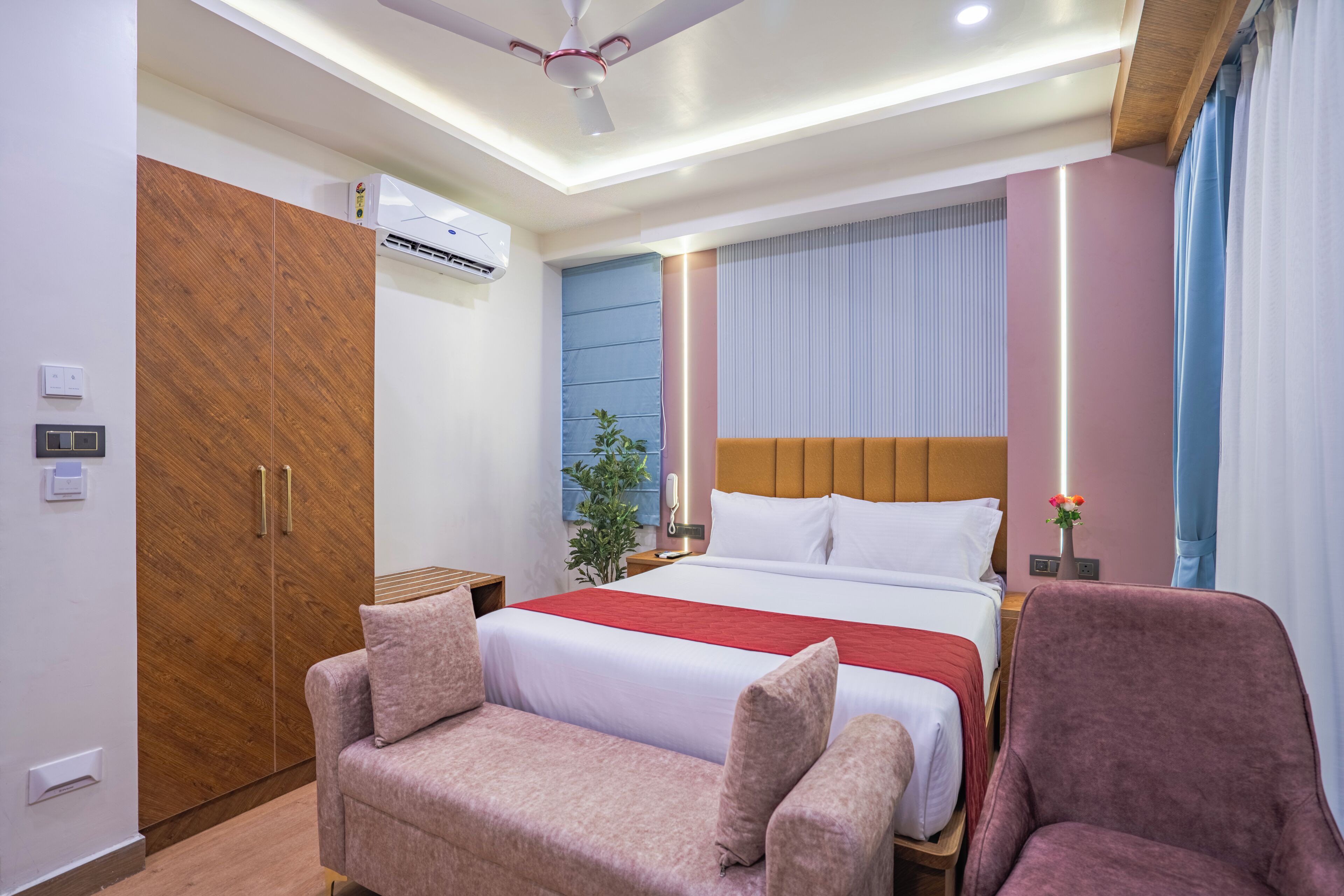 Quarto de hotel com cama, sofá, poltrona, guarda-roupa e ventoinha no teto.