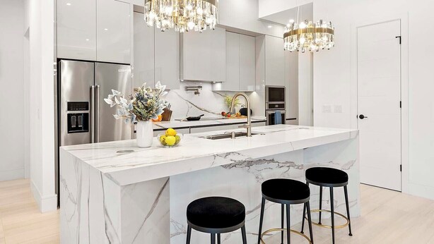 A modern kitchen with a marble island, stainless steel appliances, and black bar stools. - Bluewater- 4 bedroom, 4 bath luxury Villa - Vesteva (Cape Coral)
