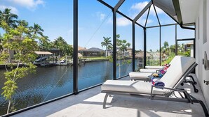 A balcony with a view of a body of water, lounge chairs, and a clear sky. - Bluewater- 4 bedroom, 4 bath luxury Villa - Vesteva (Cape Coral)