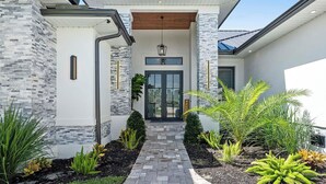 A modern house with a stone facade, a welcoming entrance, and a pathway leading to the door. - Bluewater- 4 bedroom, 4 bath luxury Villa - Vesteva (Cape Coral)