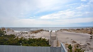 Una playa con una escalera de madera que baja a la orilla, rodeada de dunas de arena y vegetación.