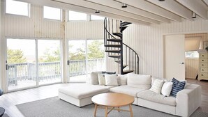 Un salón amplio con un sofá blanco moderno, una mesita redonda y una escalera de caracol.