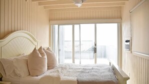 Un dormitorio con cama, almohadas, ventilador de techo y puerta corrediza de vidrio que da a un balcón exterior.