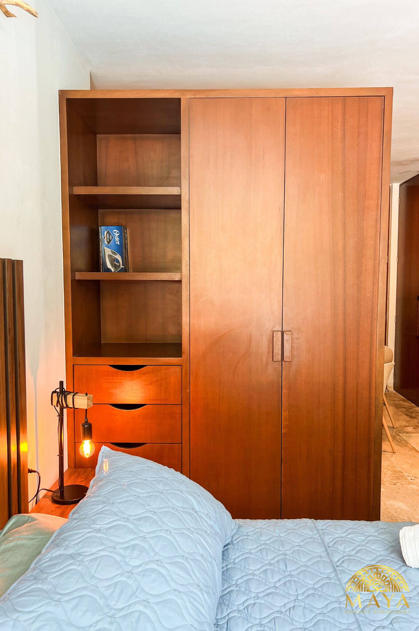 Ein Schlafzimmer mit einem Holzschrank, einem Bett mit blauer Decke und einer Nachttischlampe.