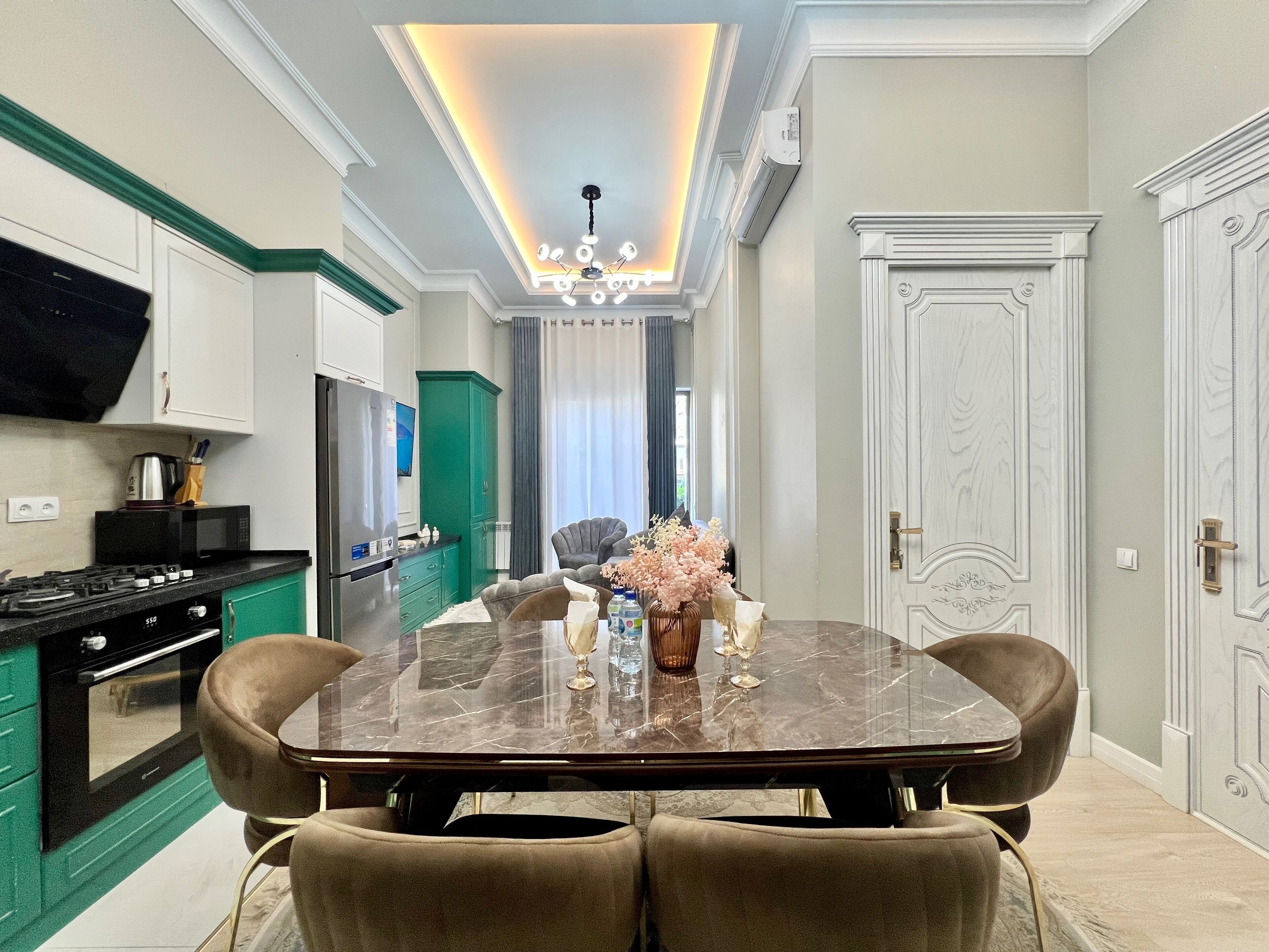 A modern kitchen with a dining area, featuring a marble table, comfortable chairs, and a chandelier.