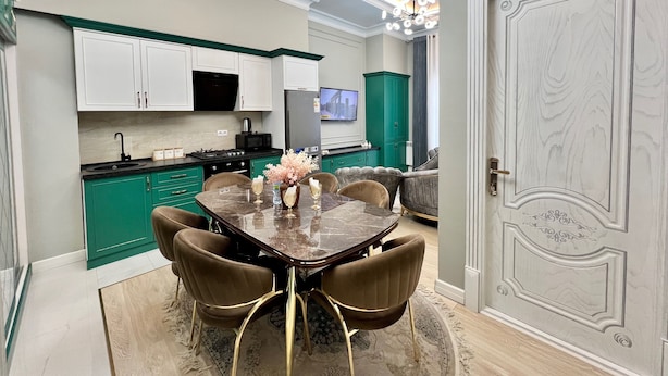Une cuisine moderne avec des meubles de couleur turquoise, un coin repas doté d’une table en marbre et de chaises rembourrées, ainsi qu’une grande porte décorative.