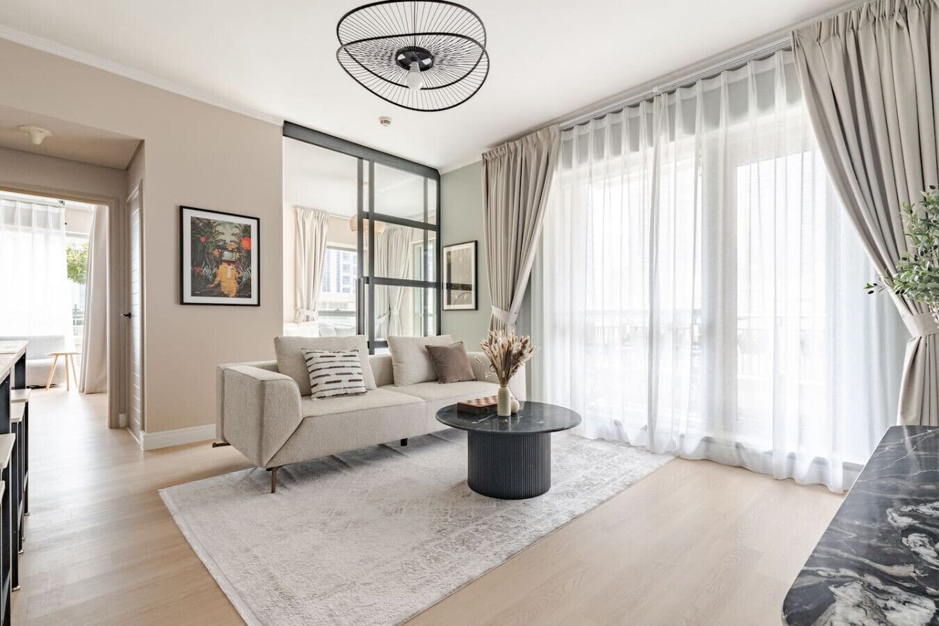Un salón moderno con un sofá, una mesa de centro y un amplio ventanal con cortinas de gasa.
