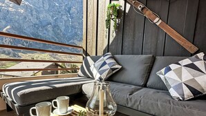 En hyggelig balkon med sofa, puder, et glasstage og krukker med planter.