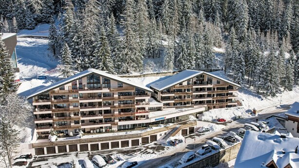 Et hotel med flere etager, altaner, en stolelift og en parkeringsplads dækket af sne.