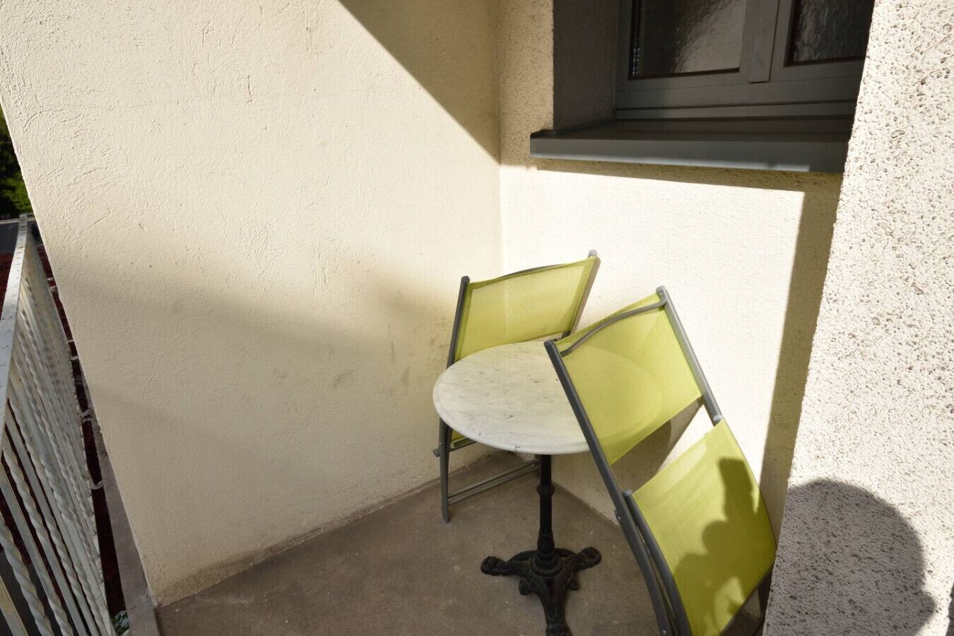 A small outdoor seating area with a table and two chairs, a metal railing, and a window.
