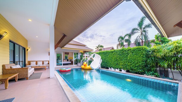 A swimming pool with a slide, outdoor seating, and lush greenery. - Natcha villa 41 (Pattaya)