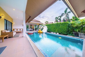 Une piscine avec un toboggan, un espace extérieur aménagé et une végétation luxuriante.