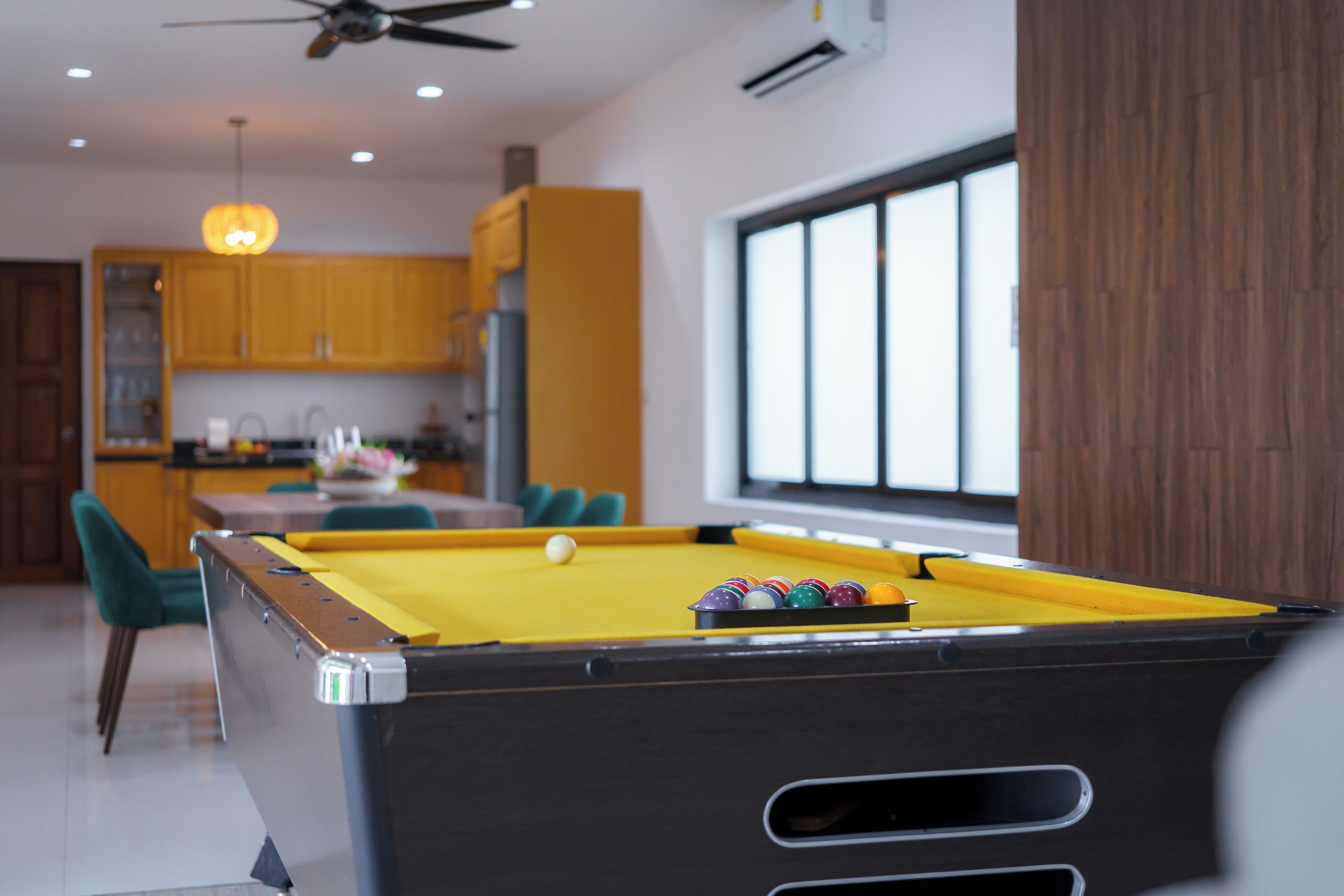 Een pooltafel in een moderne keuken met houten kasten en een groot raam.