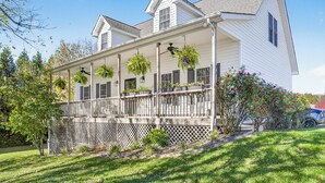 A white two-story house with a covered porch, a wooden fence, and a lawn.