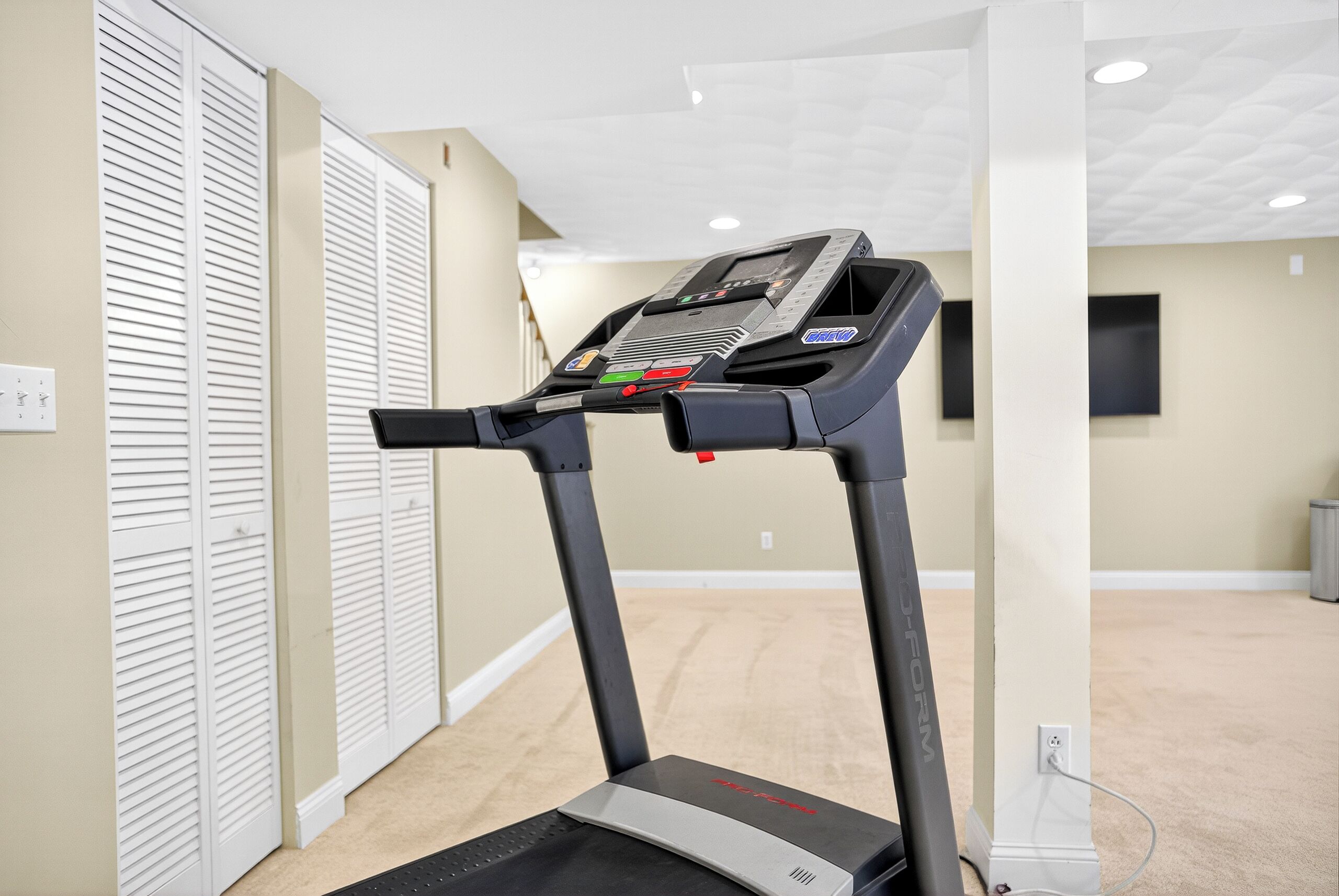Un gimnasio en casa con una cinta de correr, un armario blanco y una alfombra color beige.