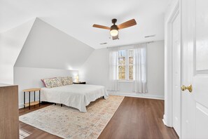 A bedroom with a bed, a nightstand, a bedside table, a ceiling fan, and a window with curtains.