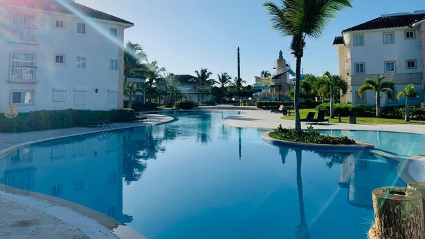 A resort pool area with a clear blue pool, palm trees, and multi-story buildings with balconies. - Studio with beach and pool access at Club Cadaqués, Bayahibe (San Rafael de Yuma)