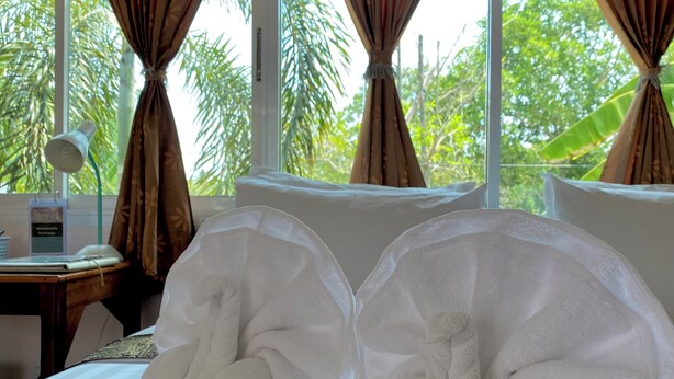 Ein Hotelzimmer mit einem Bett, zwei großen weißen Handtüchern, einem Schreibtisch mit Lampe und Blick ins Grüne durch das Fenster.