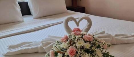 Una cama con sábanas blancas, una decoración de cisne con forma de corazón y un arreglo floral sobre la cama.