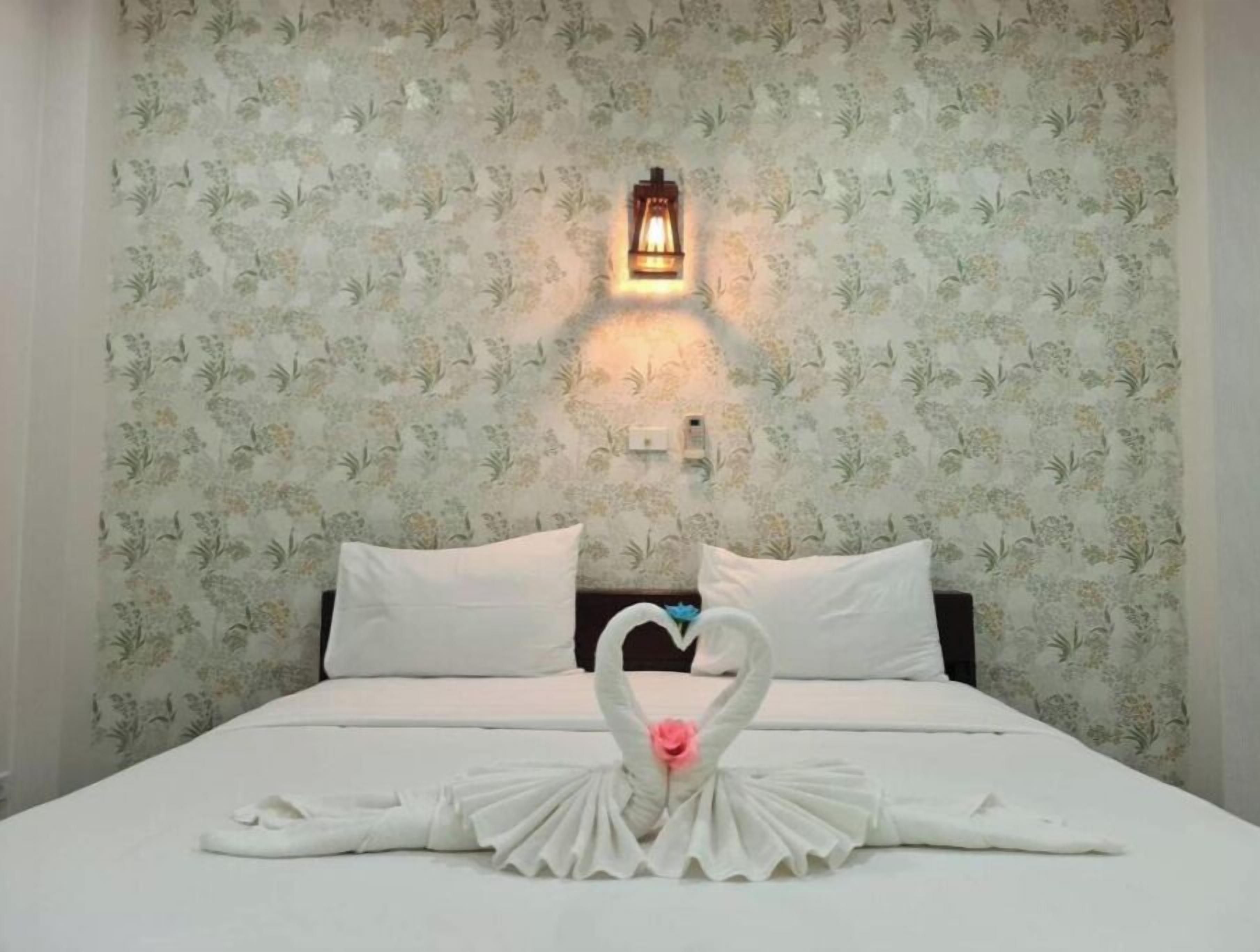 Habitación de hotel con papel tapiz floral, una cama con ropa blanca y un cisne decorativo hecho con toallas sobre la cama.