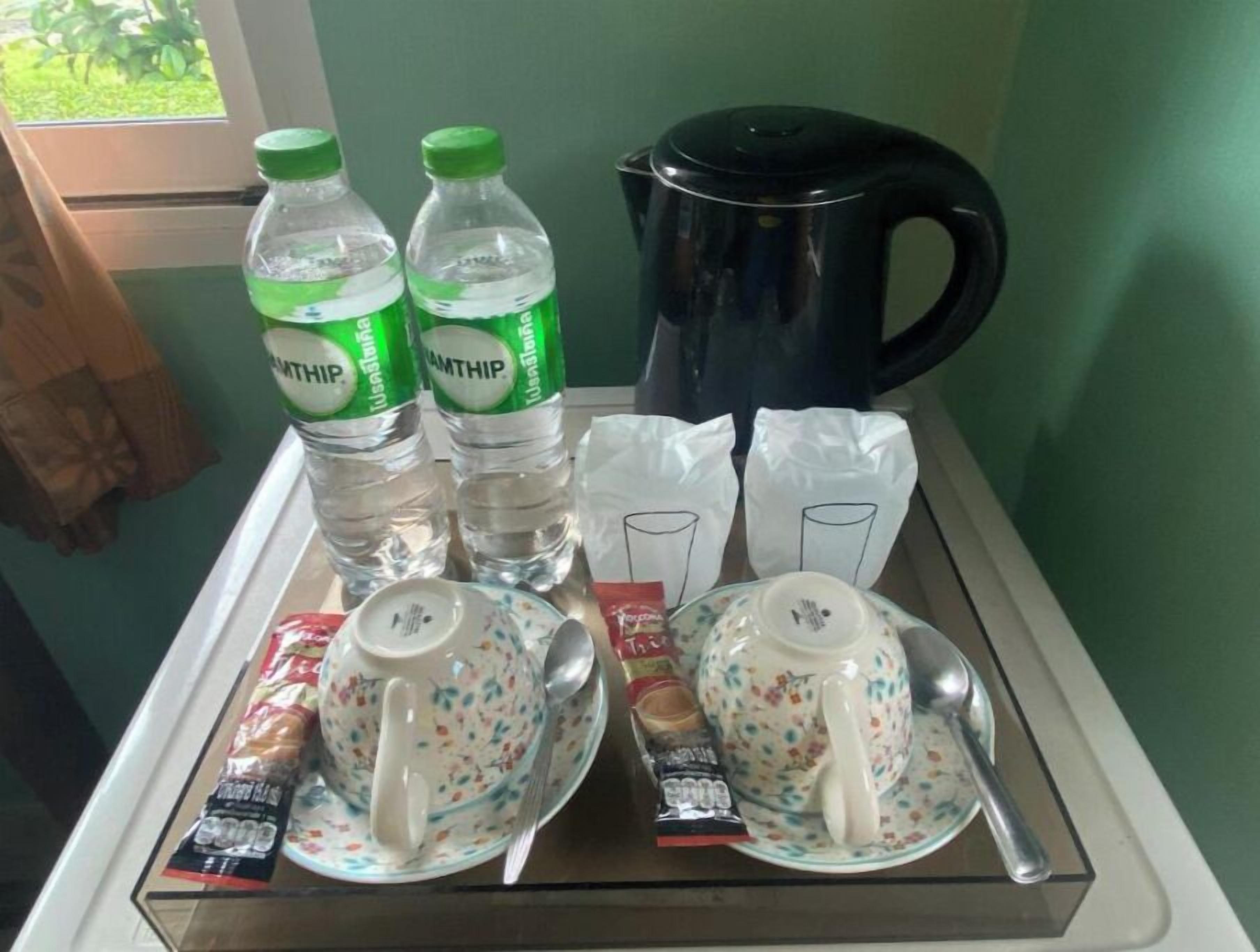Ett bricka med två flaskor vatten, en svart vattenkokare, två tekoppar med tillhörande fat, två tekoppar med teskedar och två tekoppar med ett paket snacks.