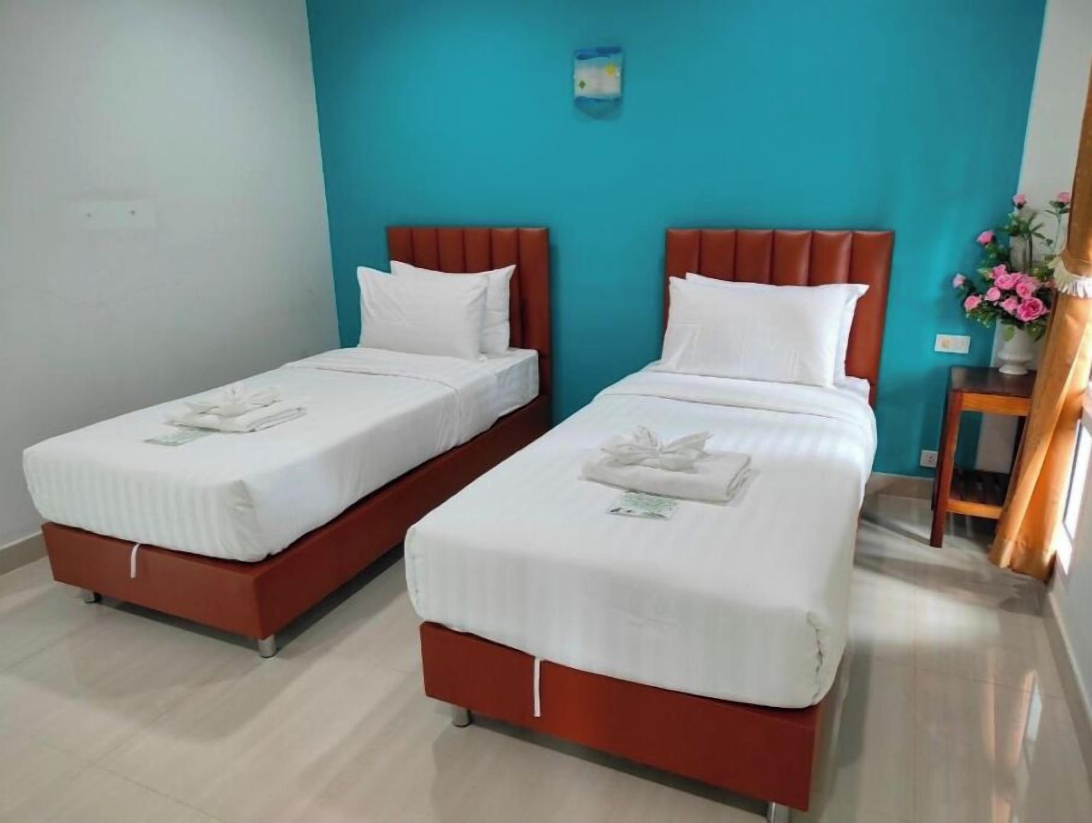 Two twin beds with white linens and red headboards in a room with teal walls.