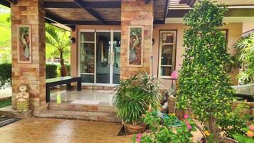 A covered patio with stone pillars, a bench, and potted plants.