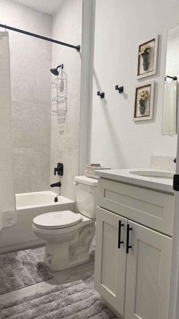 A bathroom with a toilet, bathtub, and shower. There are framed pictures on the wall and a towel rack.