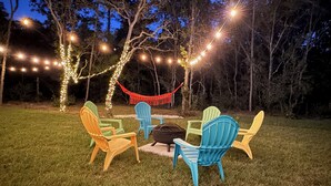 Un área de estar al aire libre con sillas Adirondack, un brasero y luces colgantes.