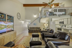 A spacious living room with a flat-screen TV, leather sofas, a plaid sofa, and a wooden cabinet. A staircase leads to an upper level with a balcony. - Last-Min Summer Escape! 15% Off Your August Stay. Must Book By 8/17/26. (Pagosa Springs)