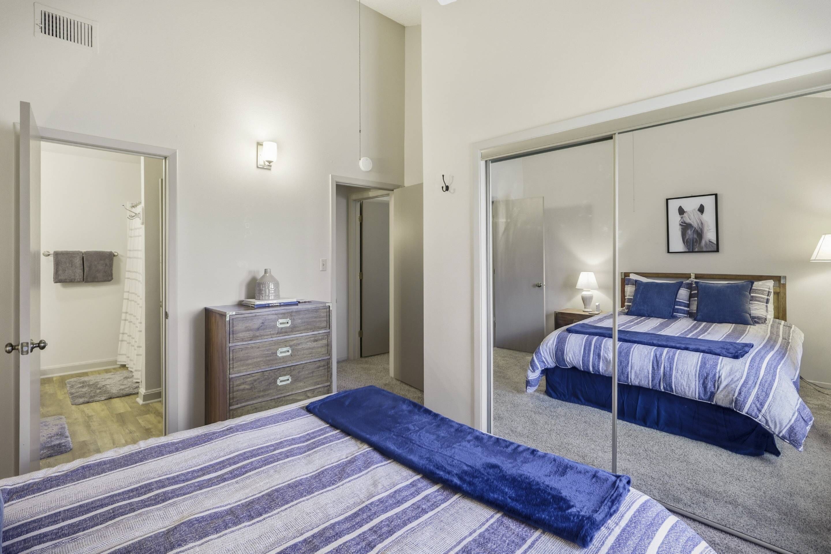 A bedroom with a bed, a dresser, a mirror, and a door leading to another room.