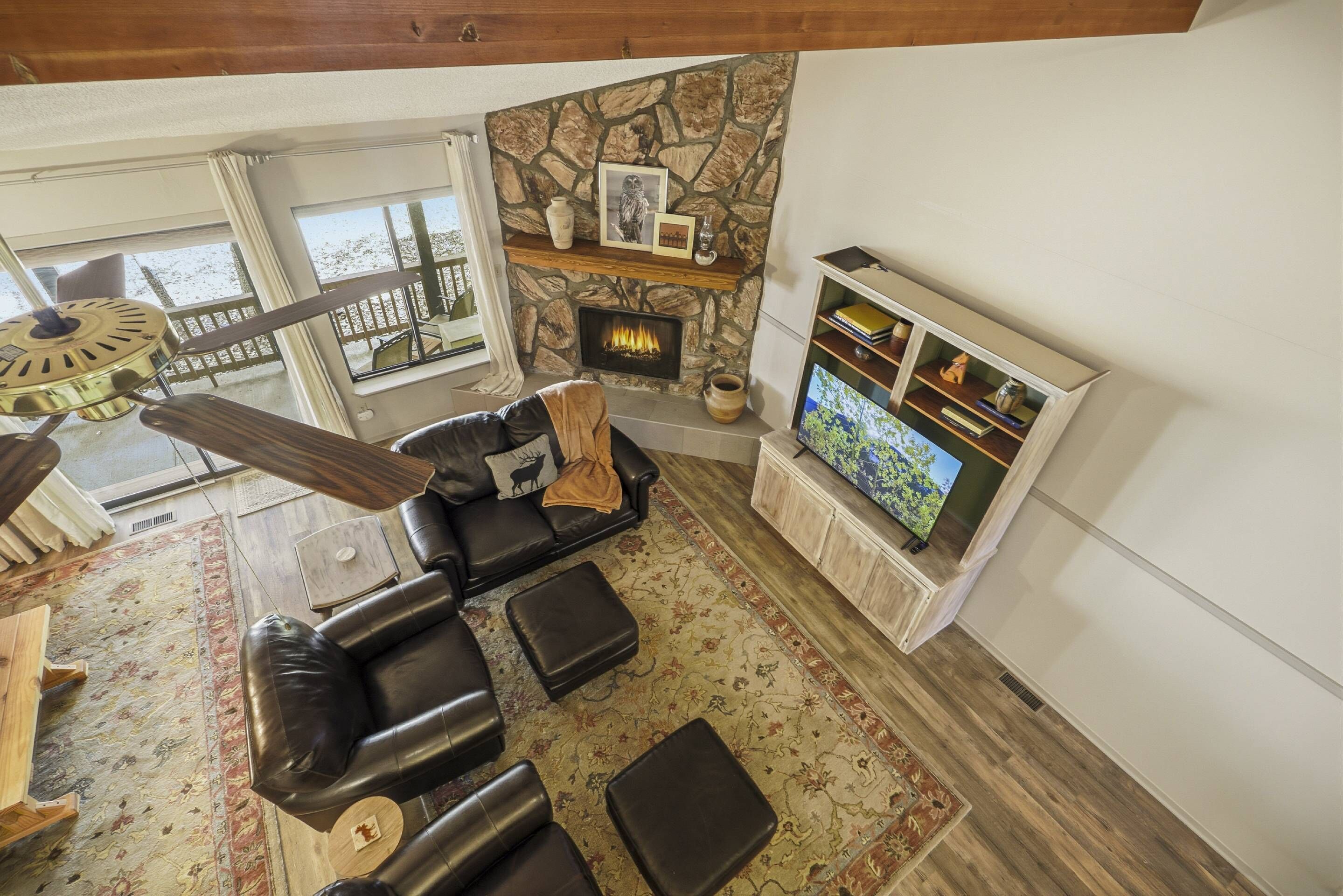 A living room with a stone fireplace, a black leather sofa, a television, and a wooden ceiling.