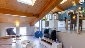 Ein modernes Wohnzimmer mit großem Fernseher, Holzbalkendecke, einer Couch und einem Essbereich.