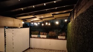 Uma área de pátio ao ar livre com piso estampado, um espaço de estar e plantas em vasos sobre uma plataforma elevada.