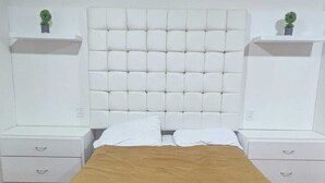 Quarto moderno com cabeceira estofada, espalha cama marrom e mesas de cabeceira brancas com gavetas.