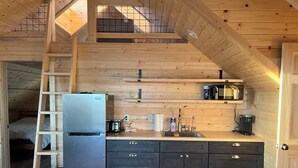Eine kleine Küche mit Kühlschrank, Spüle und Holzschränken. Eine Leiter führt zu einem Schlafbereich auf dem Dachboden.