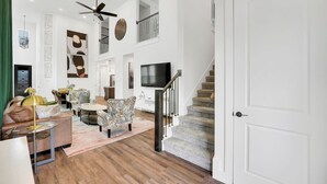 Un vaste espace de vie comprenant un escalier, un téléviseur à écran plat et un ventilateur de plafond.