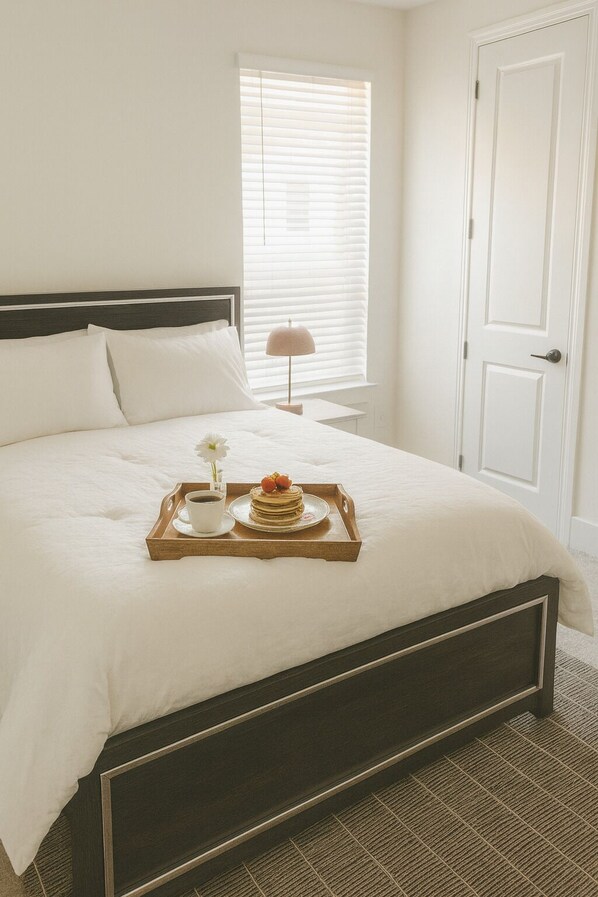 Una cama bien hecha con una bandeja de desayuno, una lámpara de noche y una ventana con persianas.