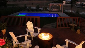 Una terraza con sillas Adirondack, un pozo de fuego y una piscina iluminada.