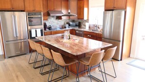 Una cocina moderna con armarios de madera, electrodomésticos de acero inoxidable, una isla de mármol y taburetes de bar.