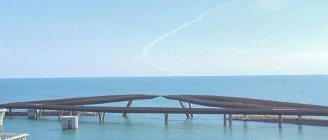 A coastal view with a bridge over water, a clear sky, and a calm sea.