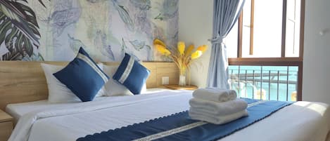 Une chambre d’hôtel avec un grand lit, une vue sur la mer par la fenêtre et une fresque murale sur le thème des tropiques.