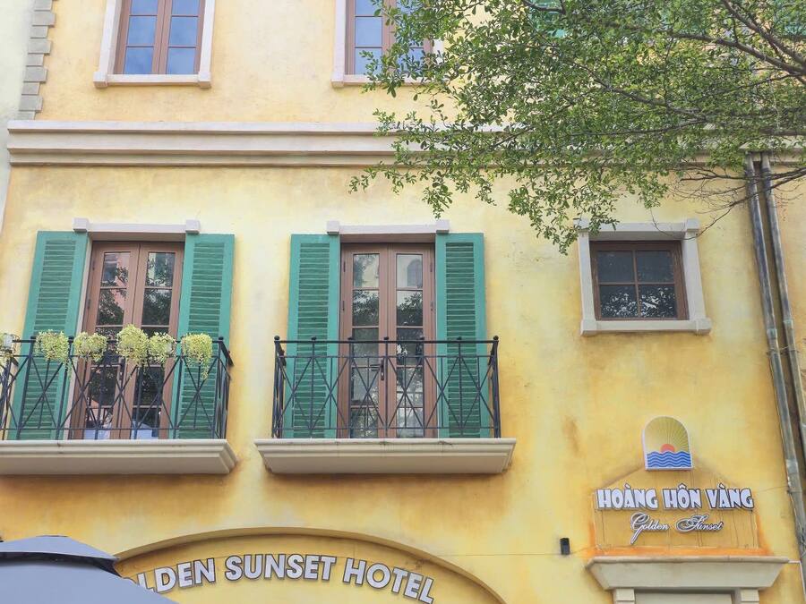 A hotel with a yellow facade, green shutters, and a sign for the Golden Sunset Hotel.