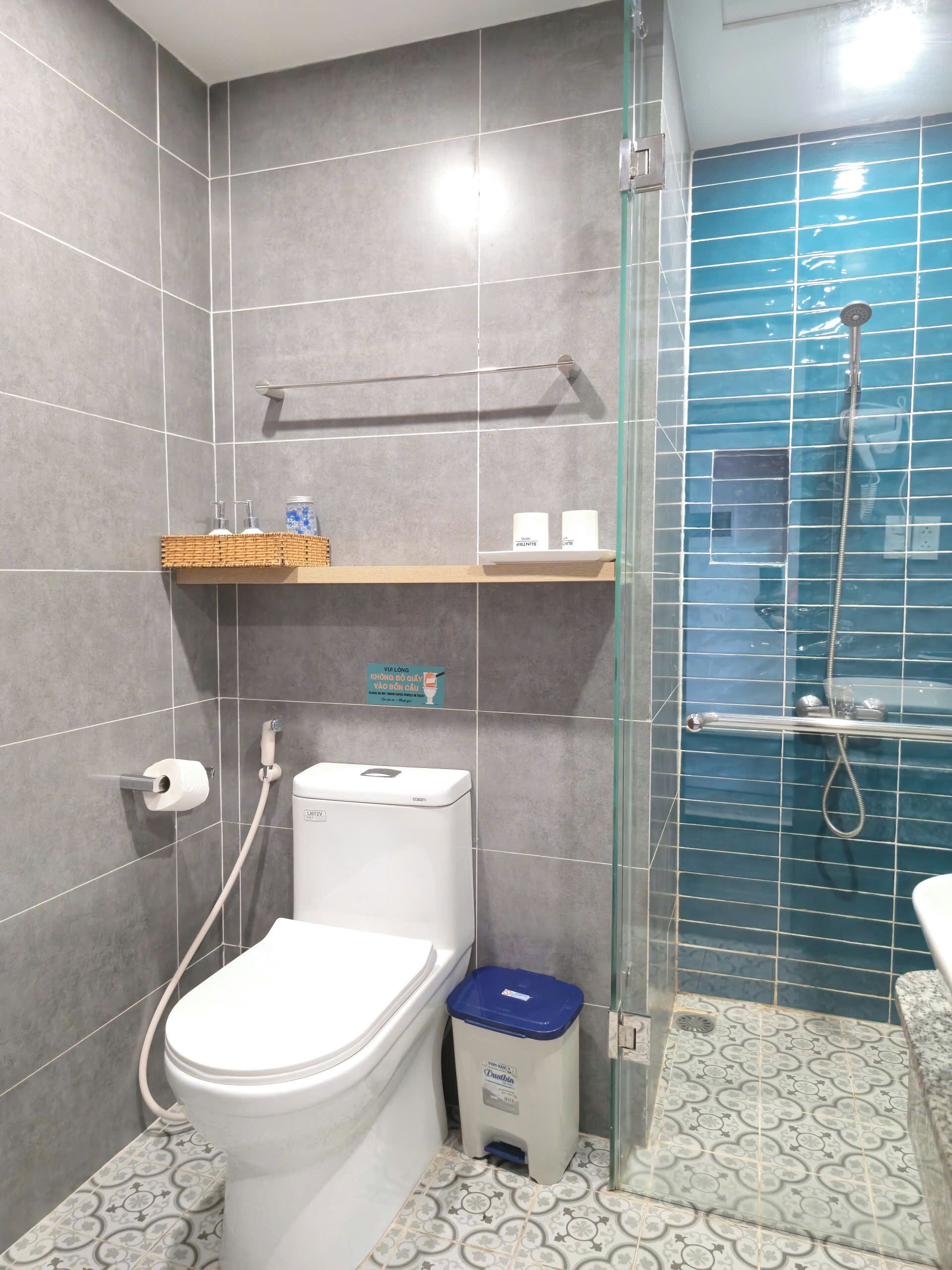 A bathroom with a toilet, a bidet, a glass shower enclosure, and a trash bin.